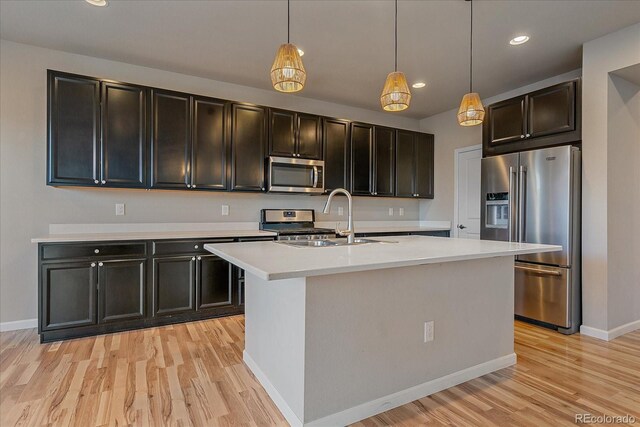 kitchen featuring sink, stainless steel appliances, a center island with sink, decorative light fixtures, and light wood-type flooring