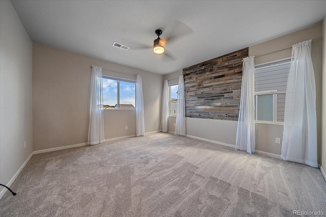 carpeted spare room with ceiling fan and wooden walls