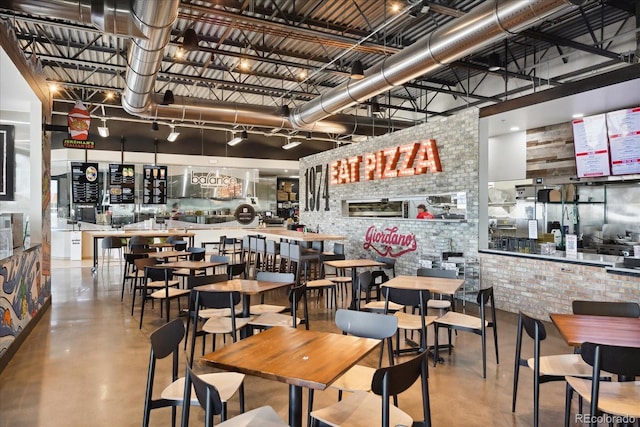 dining area with a towering ceiling, concrete flooring, and brick wall