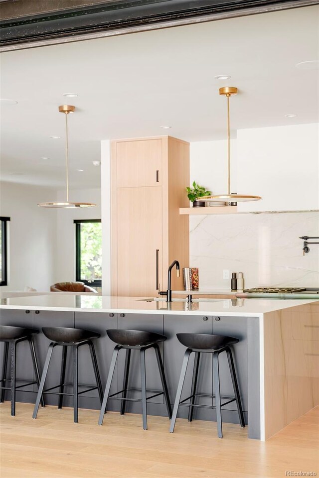 1462 S Vine St, Denver, CO 80210 - kitchen with light wood-type flooring, a breakfast bar area, decorative backsplash, stainless steel gas stovetop, and light brown cabinetry
