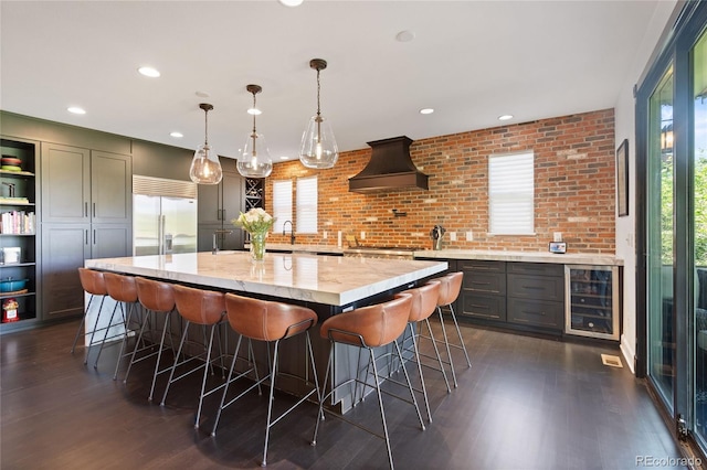 7963 S Valleyhead Way, Aurora, CO 80016 - kitchen with beverage cooler, custom exhaust hood, built in fridge, dark wood finished floors, and a kitchen breakfast bar