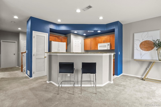 kitchen featuring a breakfast bar, white appliances, light colored carpet, and stone countertops