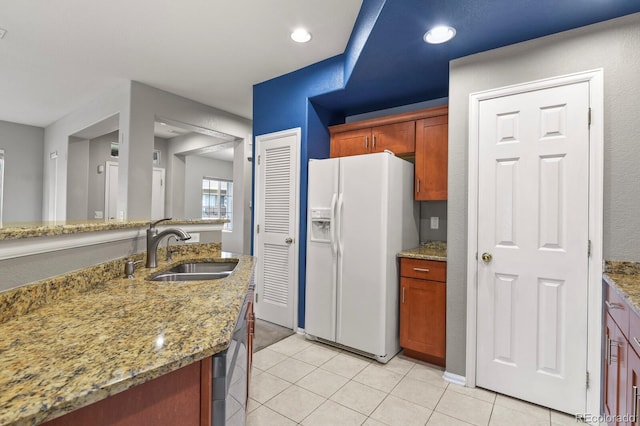 kitchen with light stone counters, white fridge with ice dispenser, light tile patterned floors, and sink