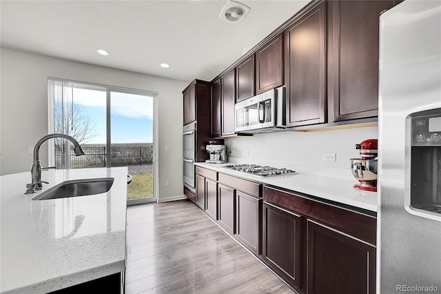 kitchen featuring sink, light wood-type flooring, dark brown cabinets, and appliances with stainless steel finishes