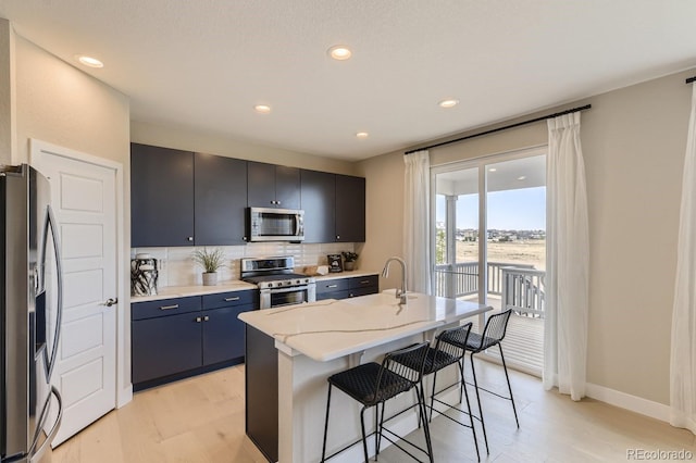 kitchen with an island with sink, a kitchen bar, decorative backsplash, stainless steel appliances, and light wood-type flooring