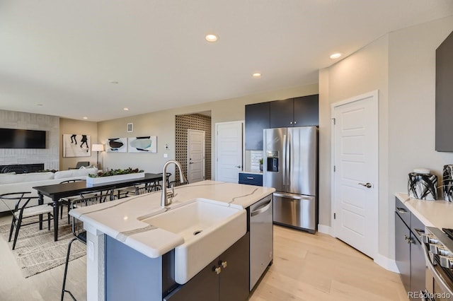 kitchen with sink, light hardwood / wood-style flooring, stainless steel appliances, a fireplace, and a center island with sink