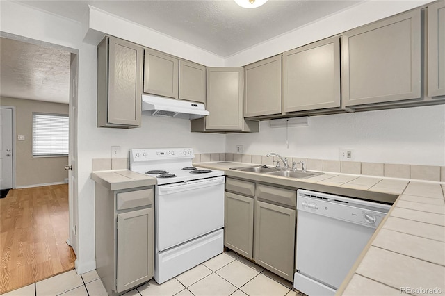 kitchen featuring tile countertops, white appliances, sink, light hardwood / wood-style flooring, and a textured ceiling