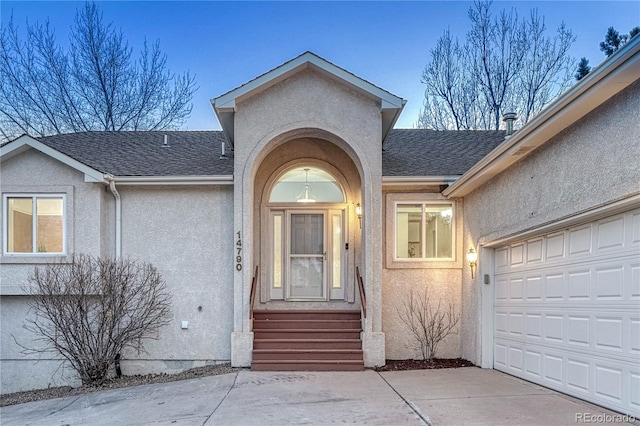 property entrance featuring stucco siding, concrete driveway, a shingled roof, and a garage