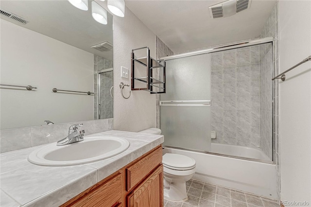 bathroom with vanity, toilet, visible vents, and combined bath / shower with glass door