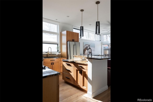 kitchen with a kitchen island with sink, high end fridge, sink, and light wood-type flooring