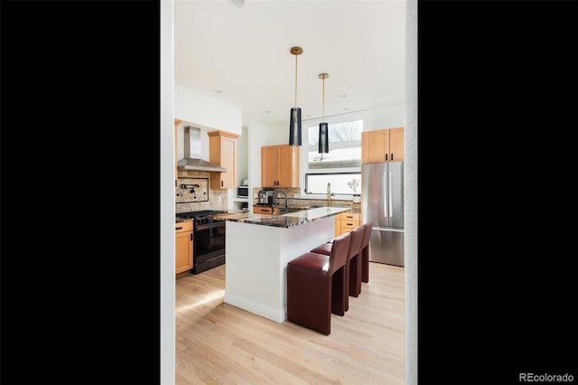 kitchen featuring wall chimney exhaust hood, gas stove, a breakfast bar area, light hardwood / wood-style flooring, and stainless steel fridge