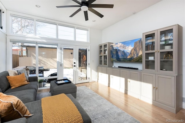 living room with french doors, a towering ceiling, a healthy amount of sunlight, and light hardwood / wood-style flooring