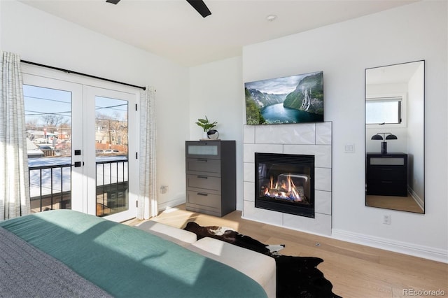 bedroom with multiple windows, a tiled fireplace, access to outside, and light wood-type flooring