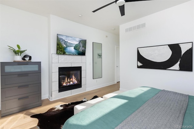 bedroom with a fireplace, light hardwood / wood-style floors, and ceiling fan