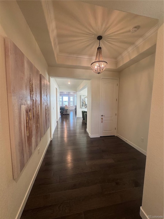 hall featuring dark wood finished floors, crown molding, a chandelier, baseboards, and a raised ceiling