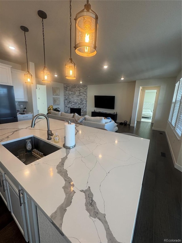 kitchen featuring a sink, a fireplace, white cabinets, light stone counters, and hanging light fixtures