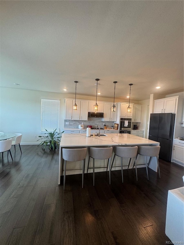 kitchen with a sink, freestanding refrigerator, dark wood-style floors, a kitchen bar, and white cabinets