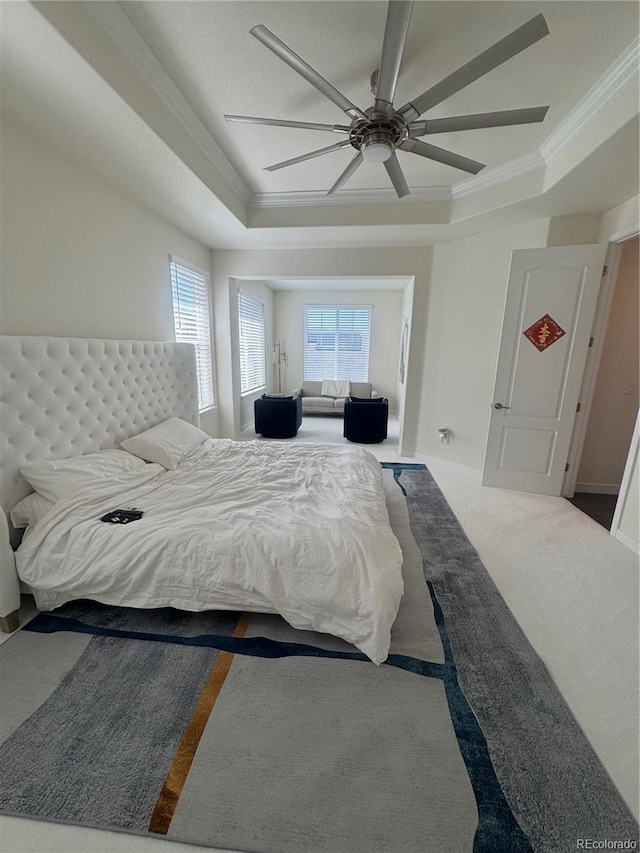 carpeted bedroom with a tray ceiling, ornamental molding, multiple windows, and ceiling fan