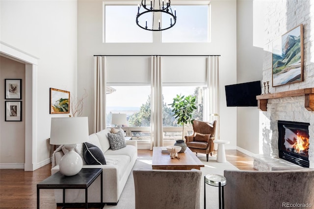 living room featuring a chandelier, a high ceiling, a stone fireplace, and hardwood / wood-style floors