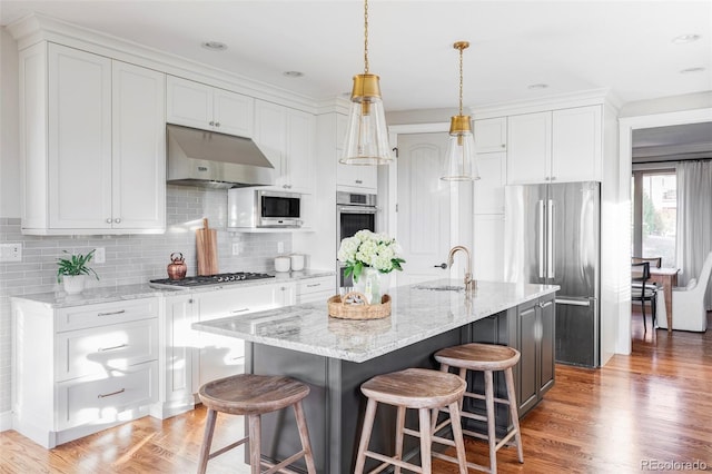 kitchen featuring decorative backsplash, stainless steel appliances, sink, white cabinetry, and an island with sink