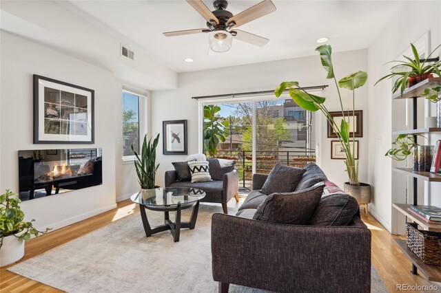 living room featuring light wood-style floors, ceiling fan, a multi sided fireplace, recessed lighting, and baseboards