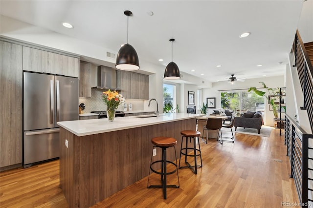 kitchen featuring stainless steel appliances, wall chimney exhaust hood, modern cabinets, a breakfast bar area, and light countertops