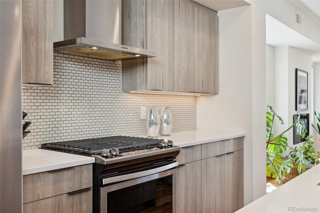 kitchen with wall chimney range hood, gas stove, modern cabinets, light countertops, and backsplash