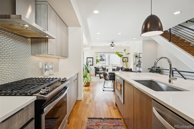 kitchen featuring appliances with stainless steel finishes, modern cabinets, a sink, wall chimney exhaust hood, and light countertops