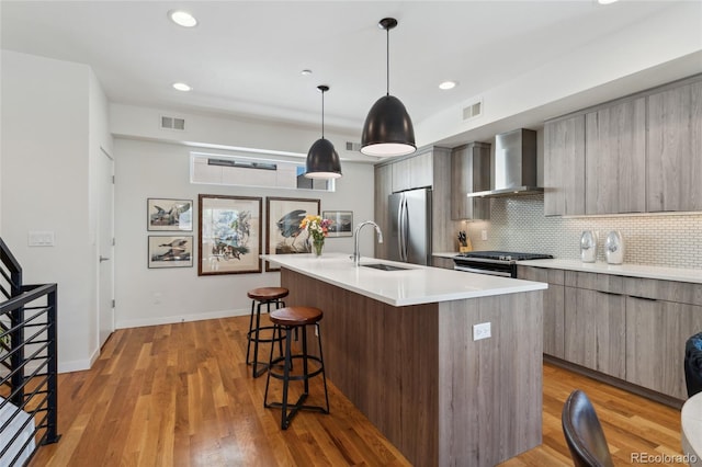kitchen featuring wall chimney range hood, modern cabinets, stainless steel appliances, a breakfast bar area, and a center island with sink