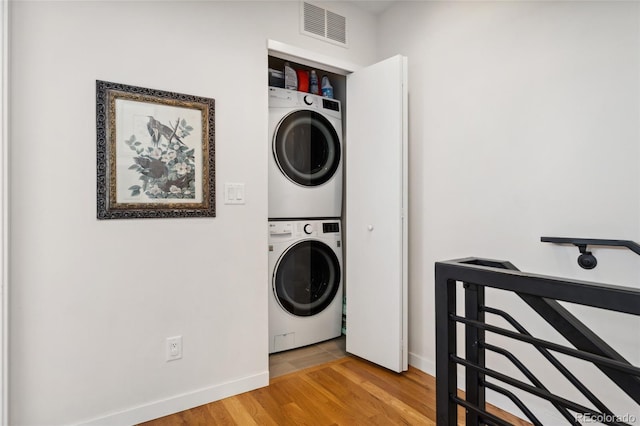 laundry area featuring stacked washer / dryer, baseboards, and light wood-style floors