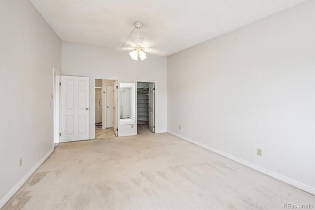 unfurnished bedroom featuring ceiling fan, a spacious closet, light colored carpet, and a textured ceiling