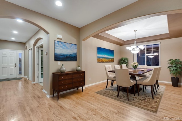 dining space featuring a raised ceiling, an inviting chandelier, and light hardwood / wood-style flooring