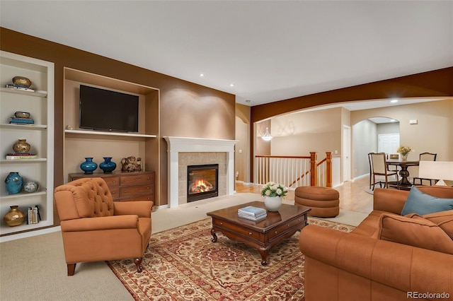 living room featuring built in shelves, light carpet, and a tile fireplace