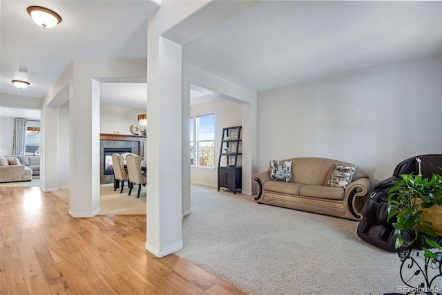 living area featuring light wood-style floors, a tile fireplace, light colored carpet, and baseboards