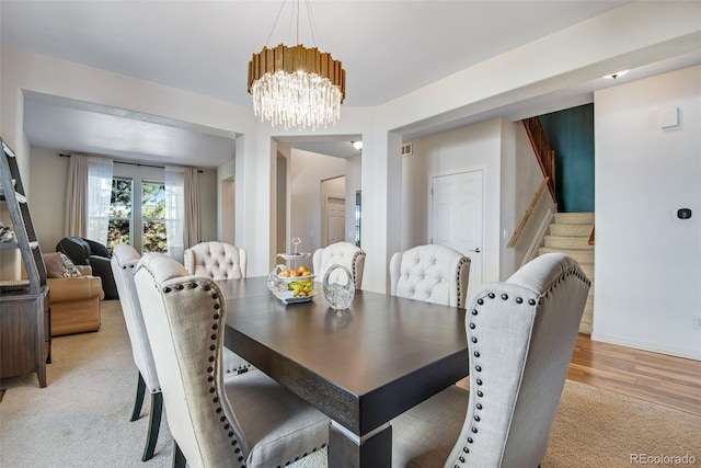 dining area with light carpet, stairway, and an inviting chandelier