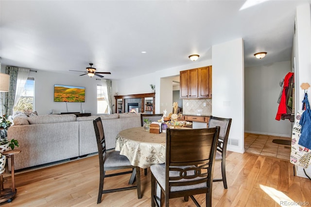 dining space with visible vents, light wood-style floors, a ceiling fan, a tile fireplace, and baseboards