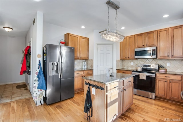 kitchen with stainless steel appliances, a center island, light wood finished floors, and light stone counters