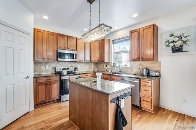 kitchen with light wood finished floors, dark stone countertops, appliances with stainless steel finishes, and a sink