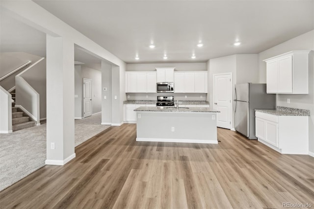 kitchen with a kitchen island with sink, light carpet, stainless steel appliances, and white cabinetry