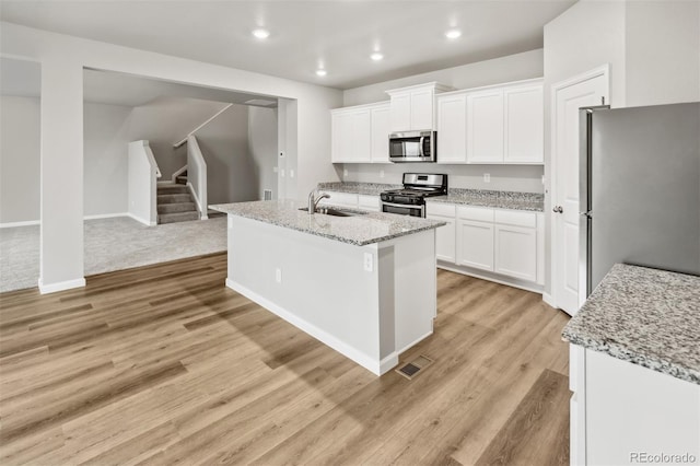 kitchen featuring white cabinetry, stainless steel appliances, a kitchen island with sink, and light wood-type flooring