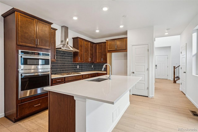 kitchen with stainless steel appliances, a kitchen island with sink, wall chimney exhaust hood, and sink