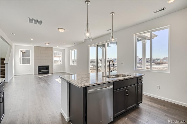 kitchen with sink, hanging light fixtures, stainless steel dishwasher, an island with sink, and light stone countertops