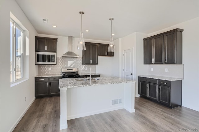 kitchen with sink, a center island with sink, stainless steel range oven, light wood-type flooring, and wall chimney exhaust hood