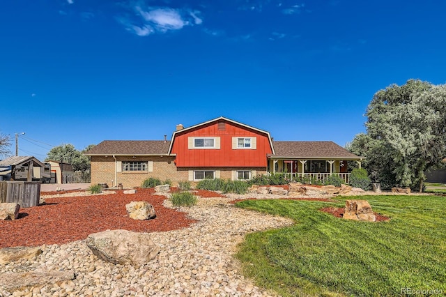 15373 Uravan St, Brighton, CO 80601 - rear view of house with a lawn, covered porch, a gambrel roof, brick siding, and roof with shingles