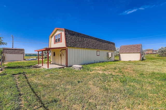 15373 Uravan St, Brighton, CO 80601 - rear view of property featuring a storage unit, roof with shingles, a lawn, and a gambrel roof