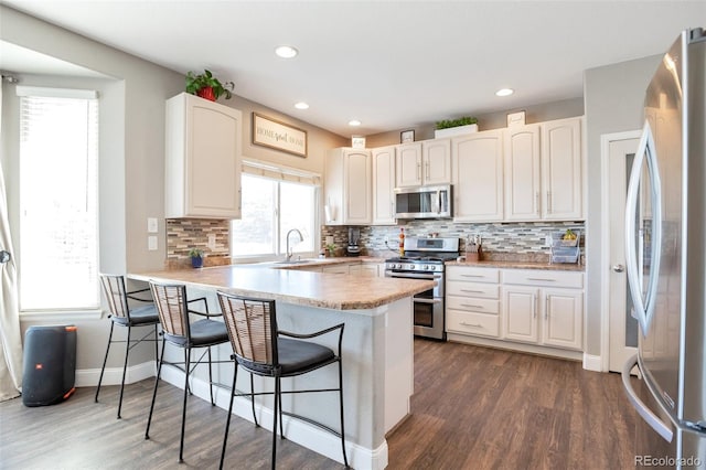 kitchen with a peninsula, appliances with stainless steel finishes, a breakfast bar area, and white cabinets