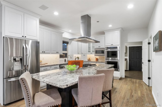 kitchen featuring light wood-type flooring, stainless steel appliances, island range hood, a kitchen island, and white cabinets