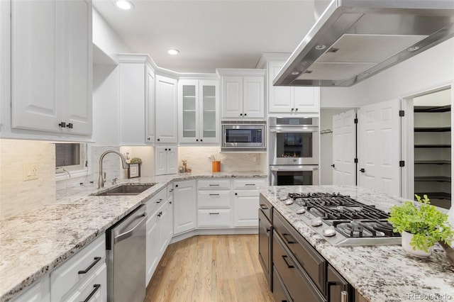 kitchen featuring light wood-type flooring, appliances with stainless steel finishes, white cabinetry, sink, and wall chimney range hood