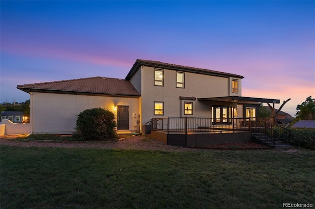 back house at dusk with central AC unit, a deck, and a lawn