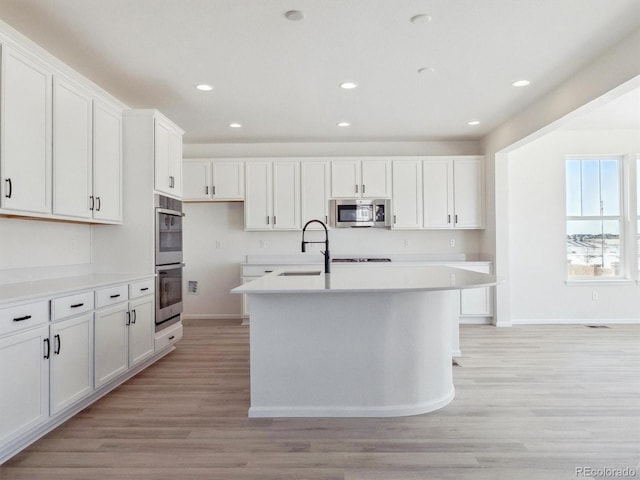 kitchen featuring white cabinets, a center island with sink, appliances with stainless steel finishes, and light hardwood / wood-style flooring